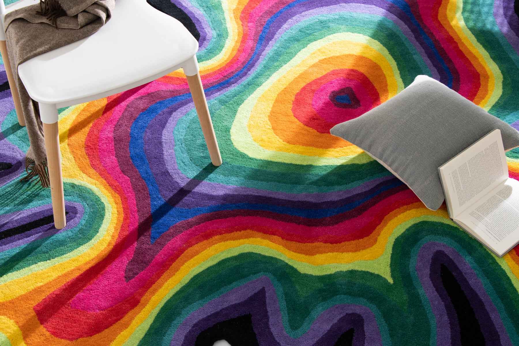 Paint Melts Rhapsody rug lifestyle shot with coffee mug and book - vibrant rainbow concentric circles hand-tufted texture