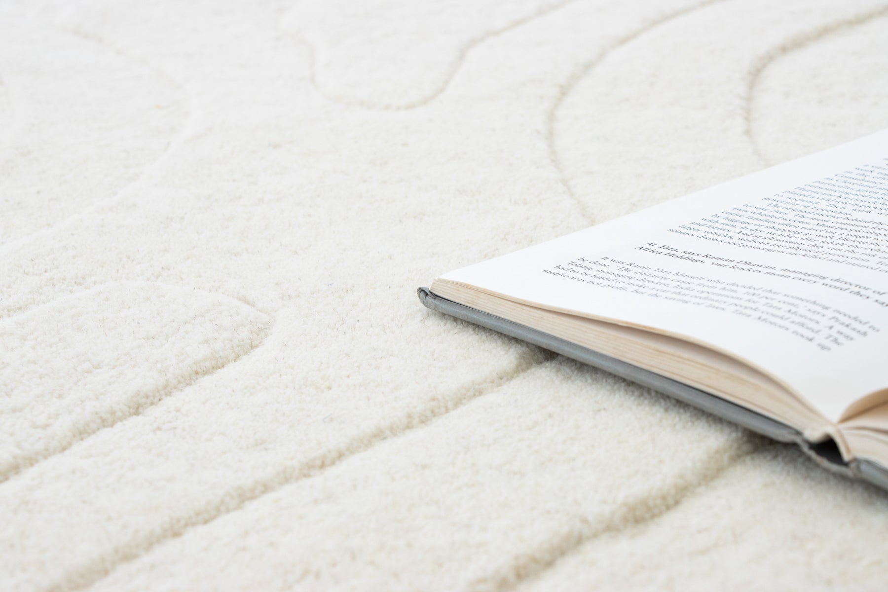 Amoeba Polar wool rug close-up with open book resting on ivory wave-pattern pile