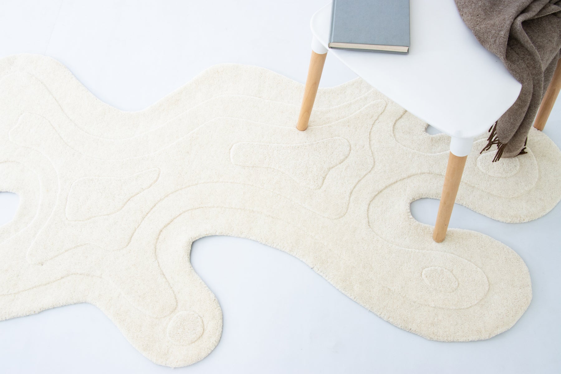 Amoeba Polar ivory rug full view with white stool and grey throw in modern room