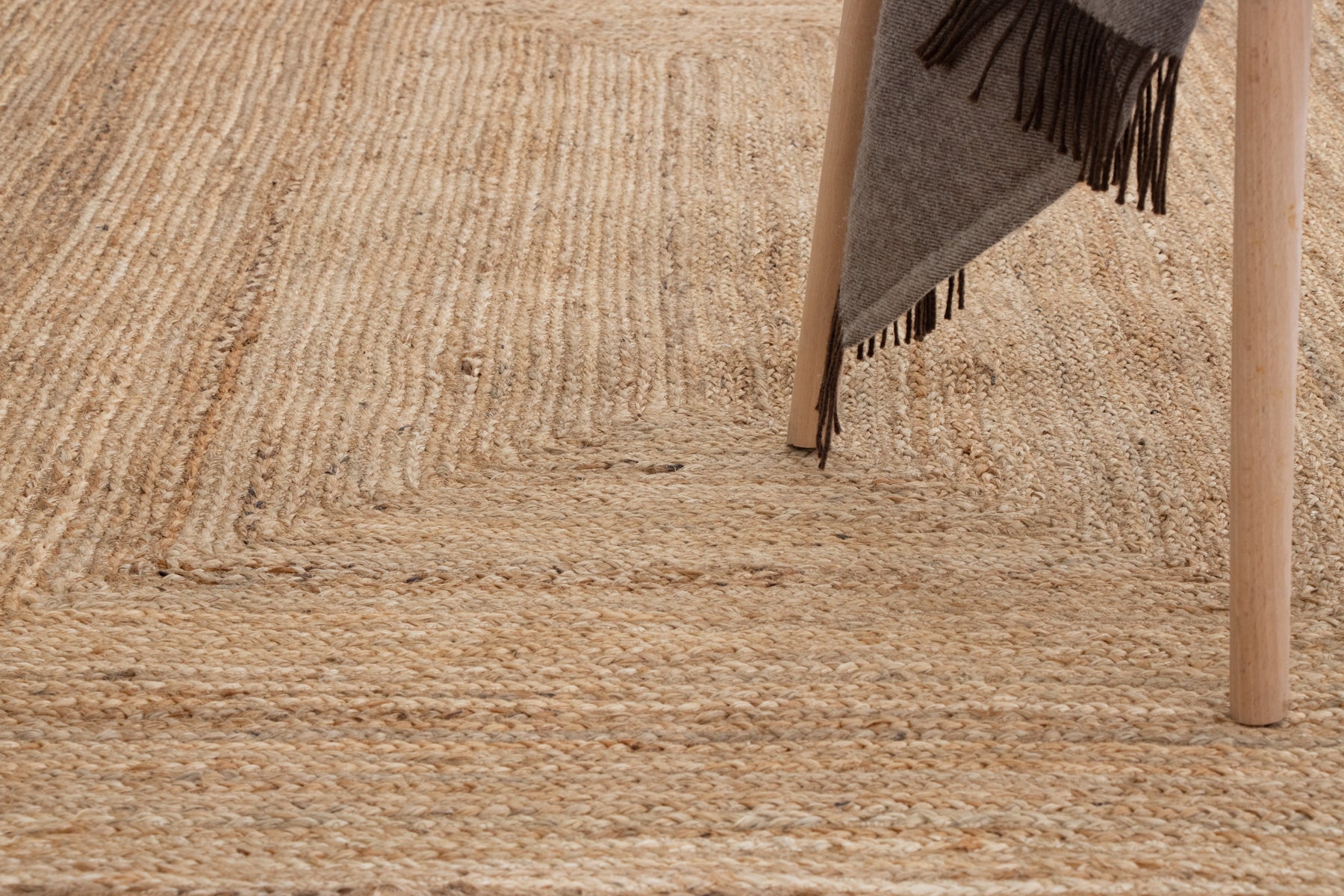 Close-up of a textured beige rug with a fringed gray blanket
