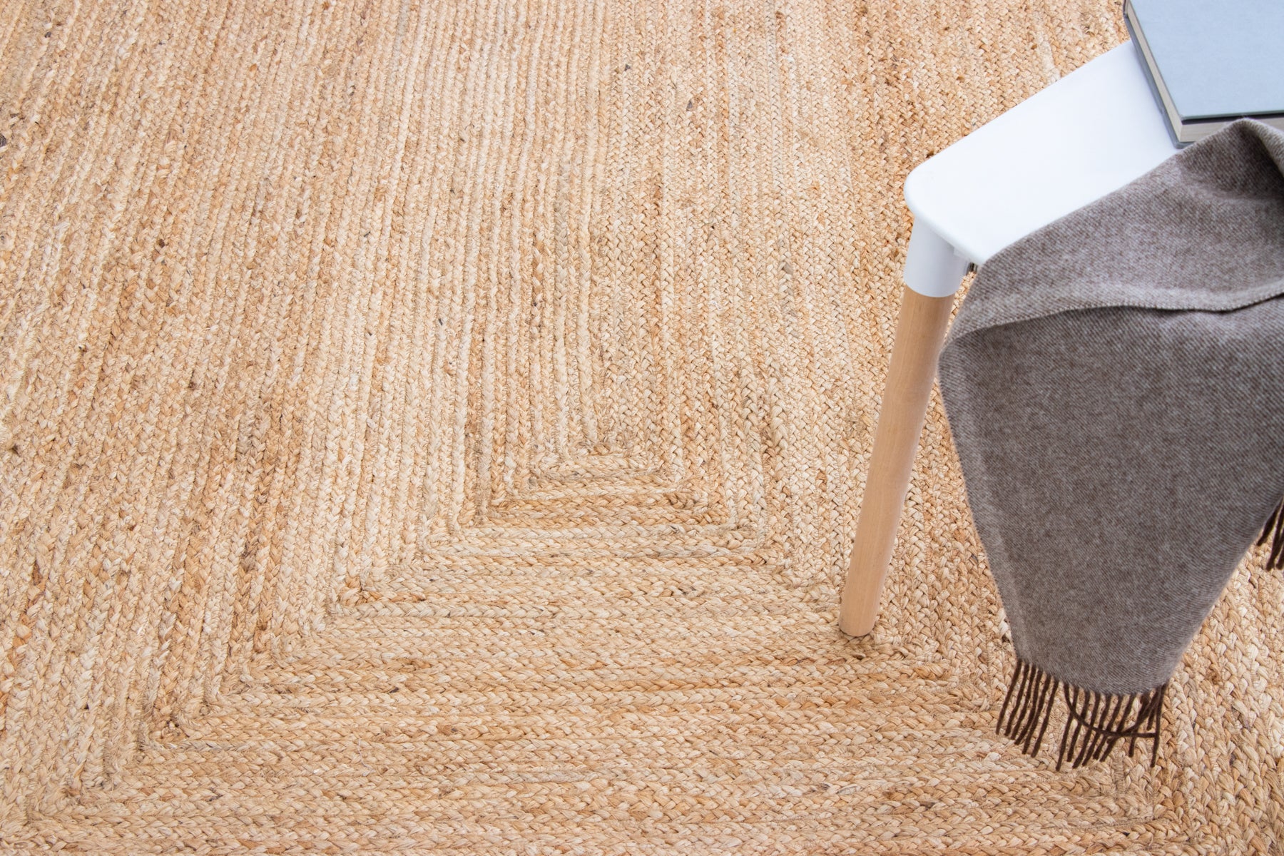 Close-up of a textured beige rug with a chair leg and gray blanket.