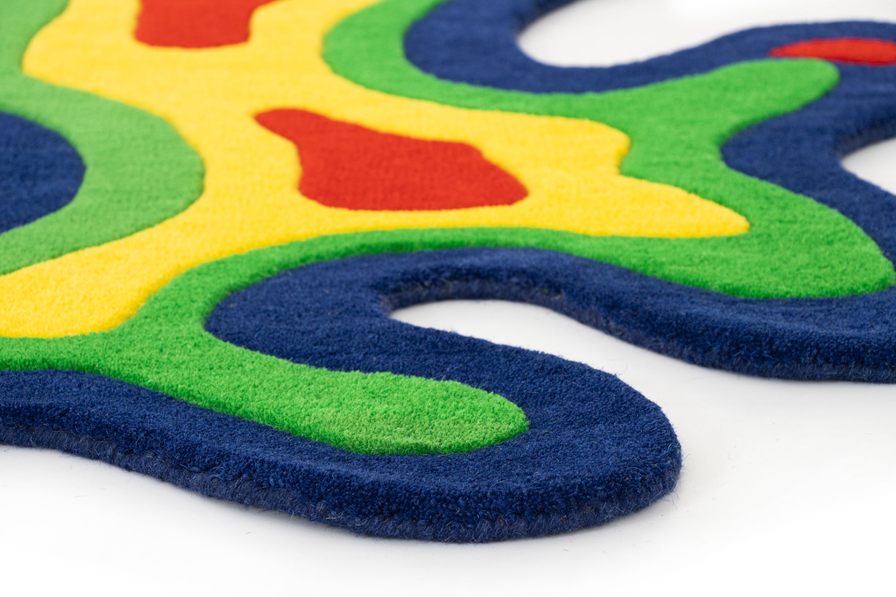 Amoeba Thermal rug corner close-up showing navy border, green, yellow and red pile | Beyond Rugs