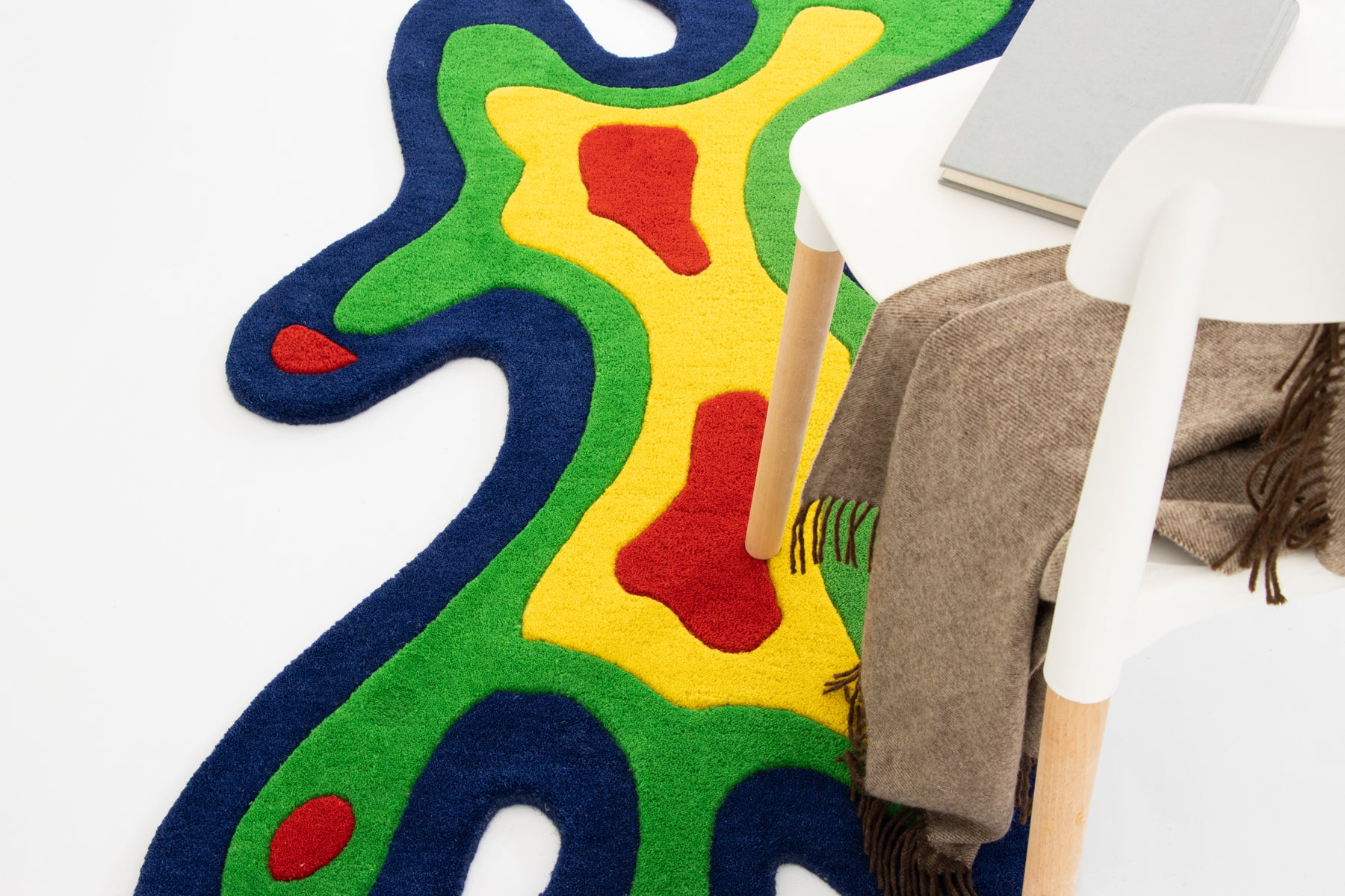 Amoeba Thermal rug leaning on white wall with wooden stool and grey throw blanket | Beyond Rugs