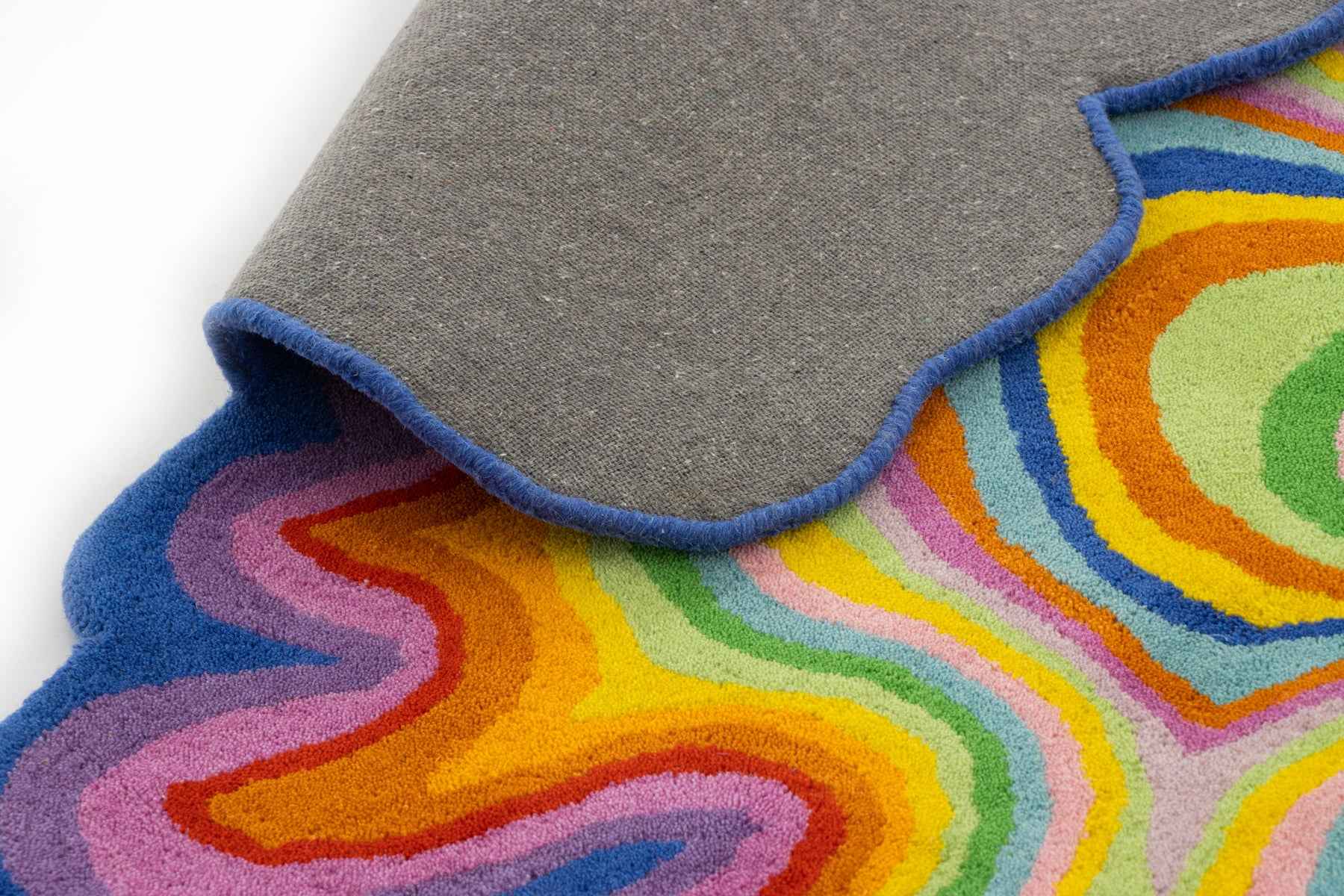 Psychedelic rug corner folded showing grey canvas backing and scalloped blue edge | Beyond Rugs