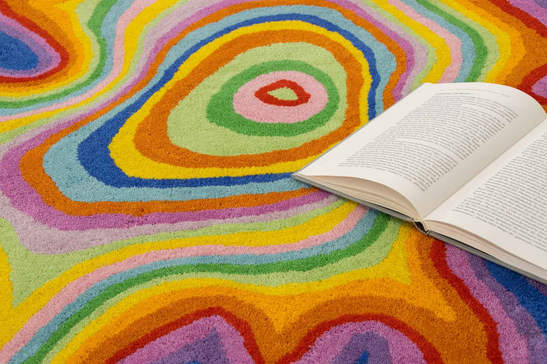 Psychedelic rug ground-level close-up with open book on rainbow swirl wool pile | Beyond Rugs
