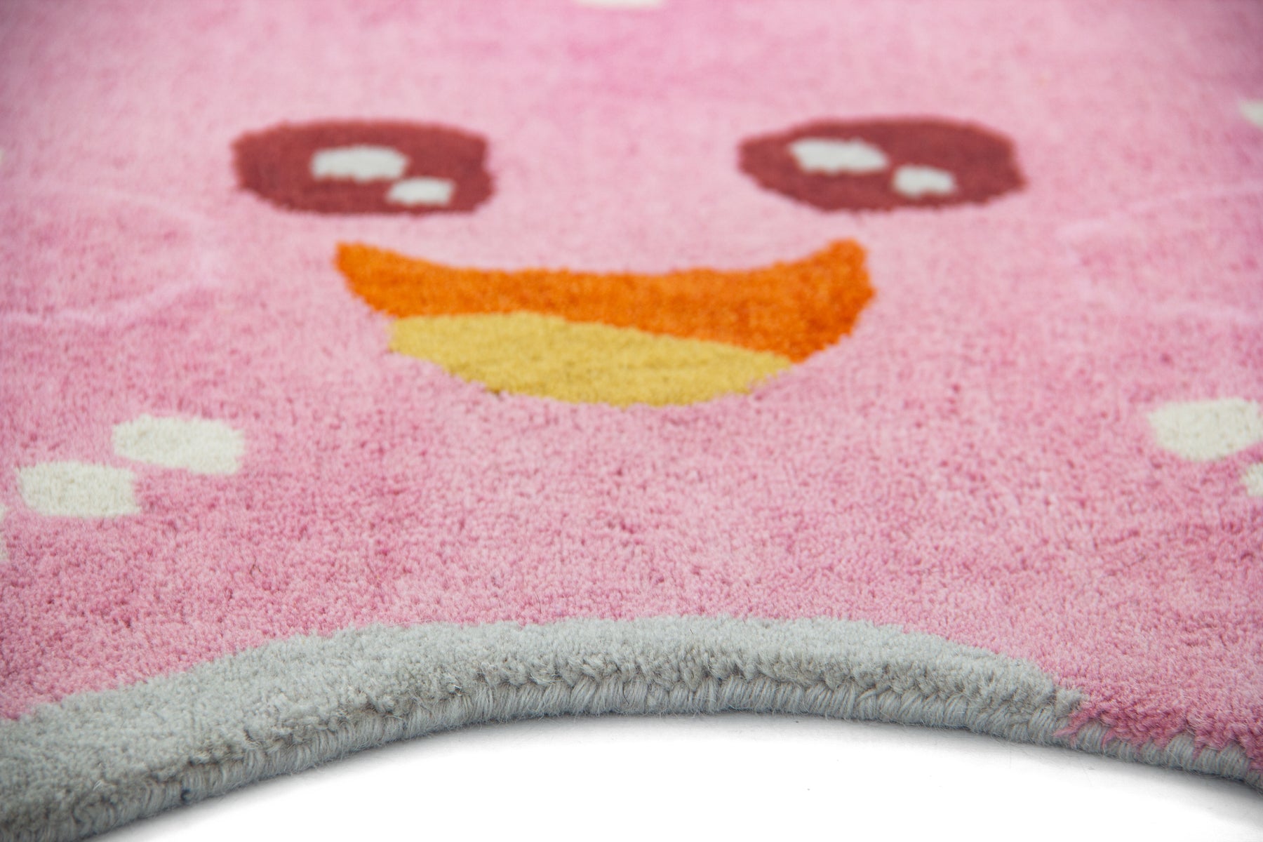 Angled view of baby pink starfish irregular rug showing smiley face and grey canvas edge | Beyond Rugs
