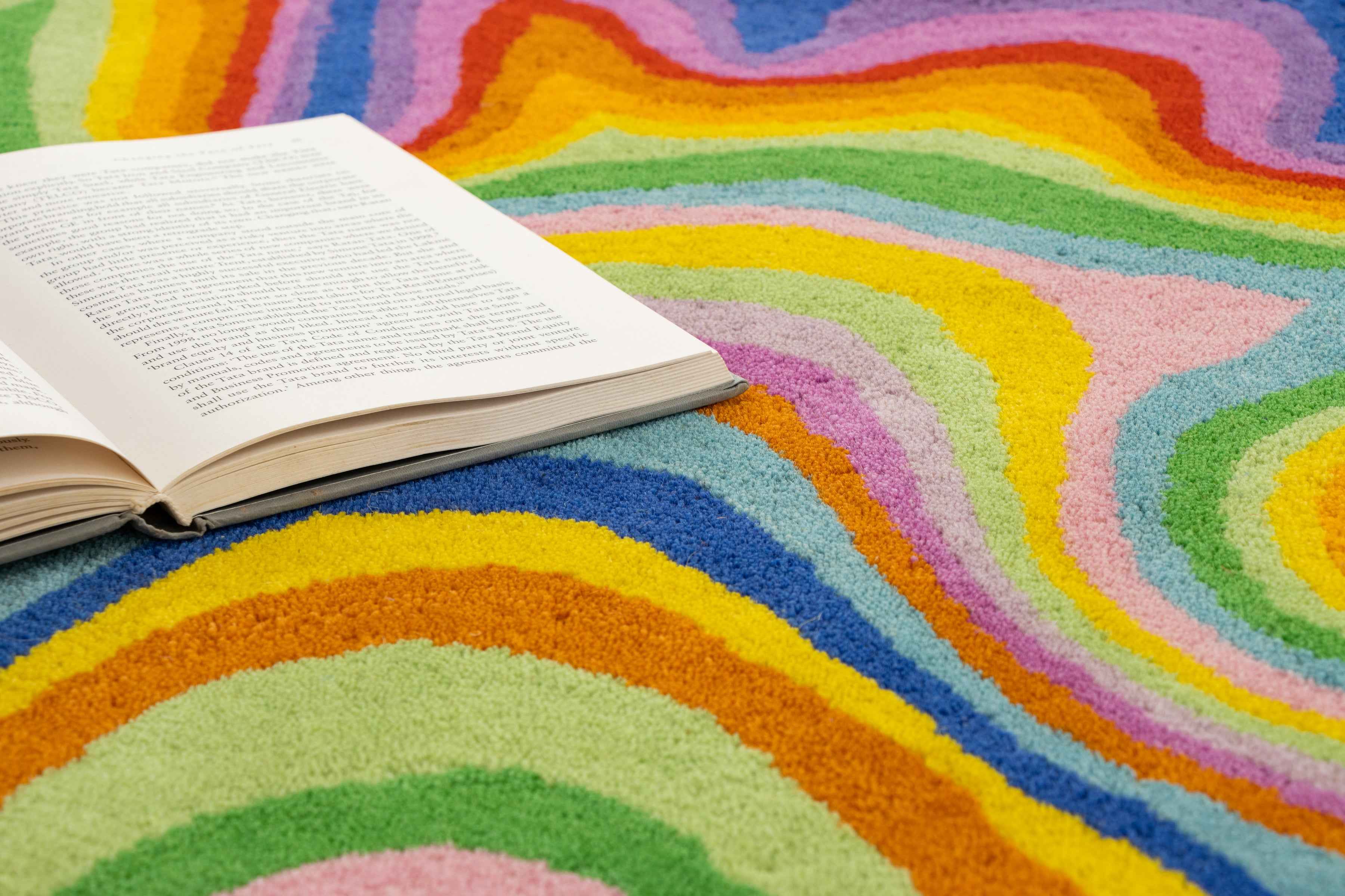 Psychedelic rug close-up with open book on green, yellow and teal swirl wool pile | Beyond Rugs