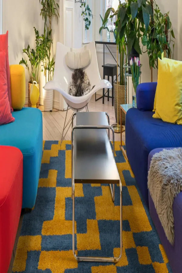 Colorful living room with blue, red, and yellow furniture on a geometric patterned rug.